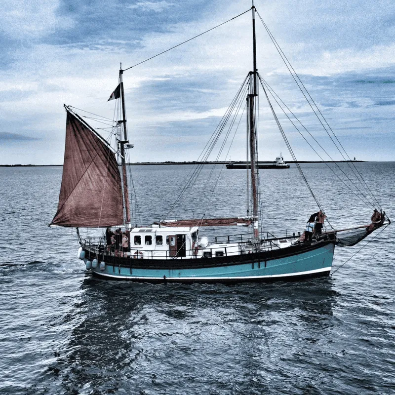 A traditional sailing vessel with brown sails underway with young crew on deck