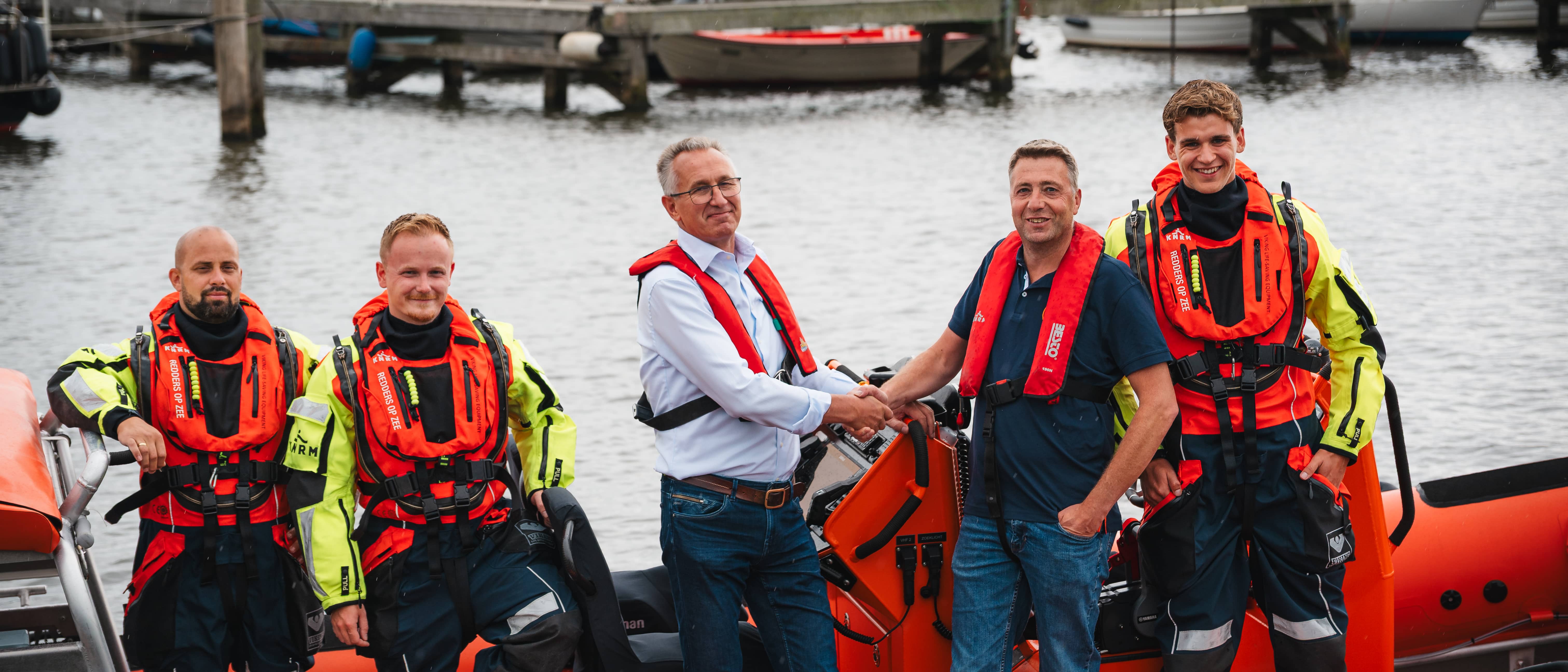 A Marad representative shaking hands with a KNRM Urk crew member at the harbour, with the rescue crew in survival suits alongside their lifeboat